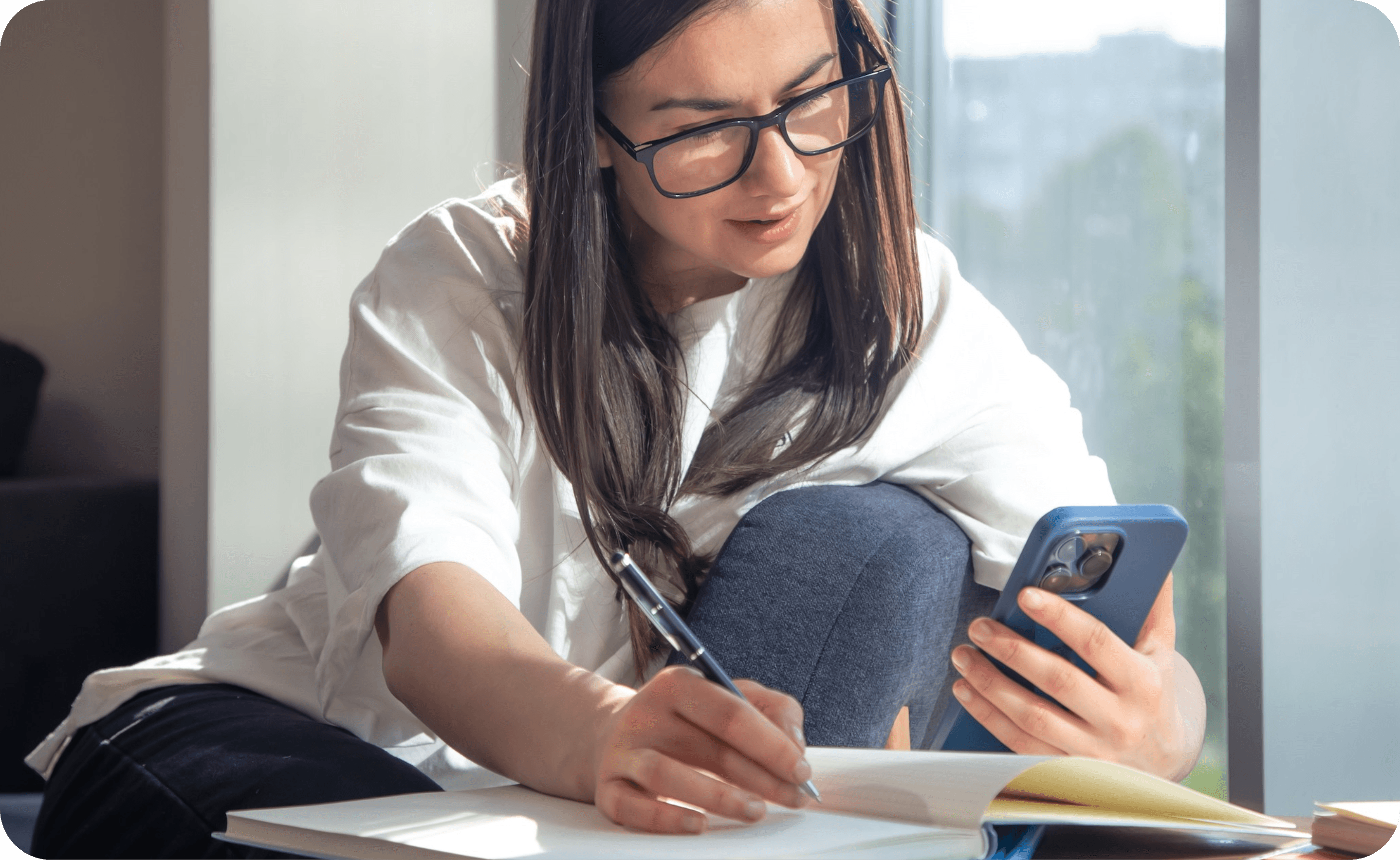 Estudiante tomando notas mientras revisa contenido desde su celular